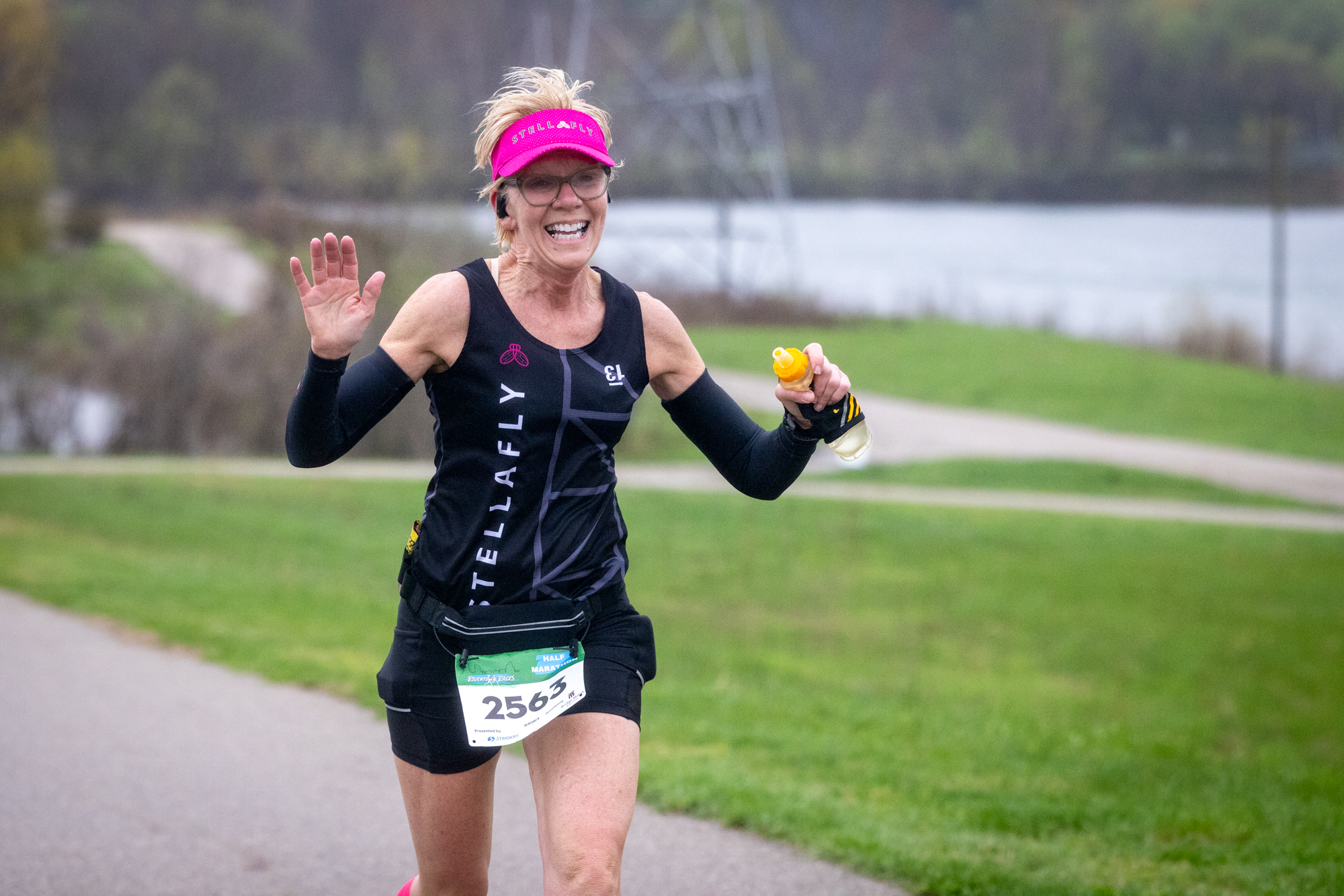 A StellaFly runner smiling and waving while racing along the river